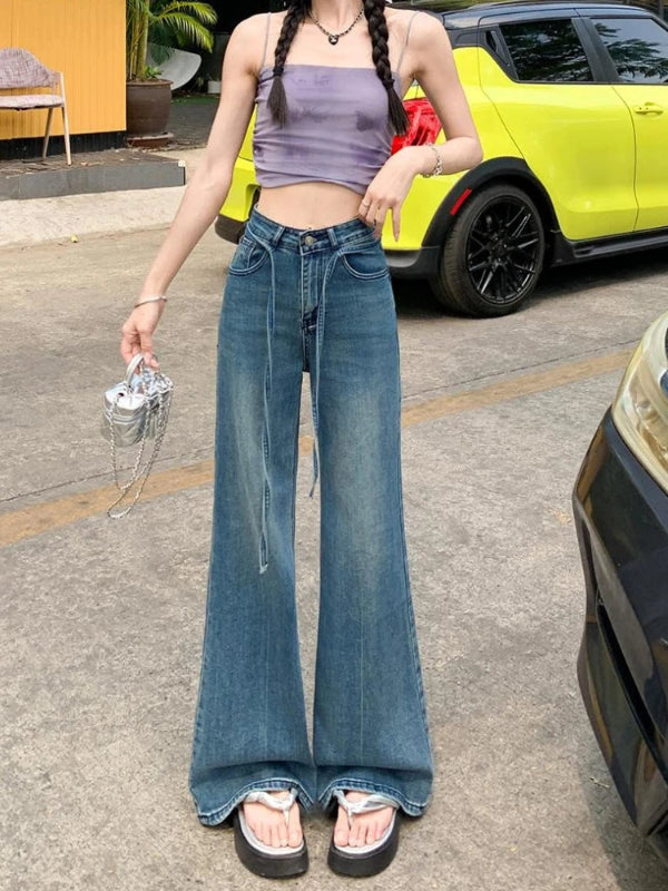 Person wearing a purple top and blue jeans standing on a street with a yellow car in the background.