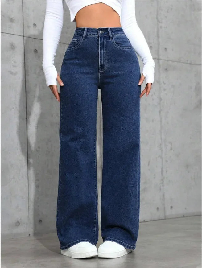 Person wearing blue wide-leg jeans and a white top against a gray concrete wall.
