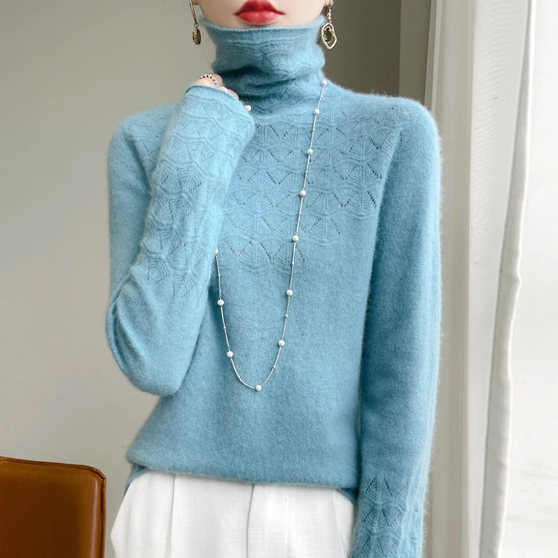 Person wearing a light blue turtleneck sweater with a long necklace, standing against a neutral background.