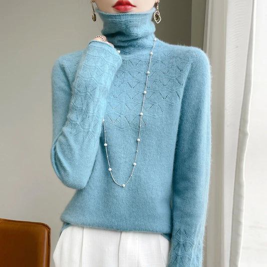 Person wearing a light blue turtleneck sweater with a long necklace, standing against a neutral background.