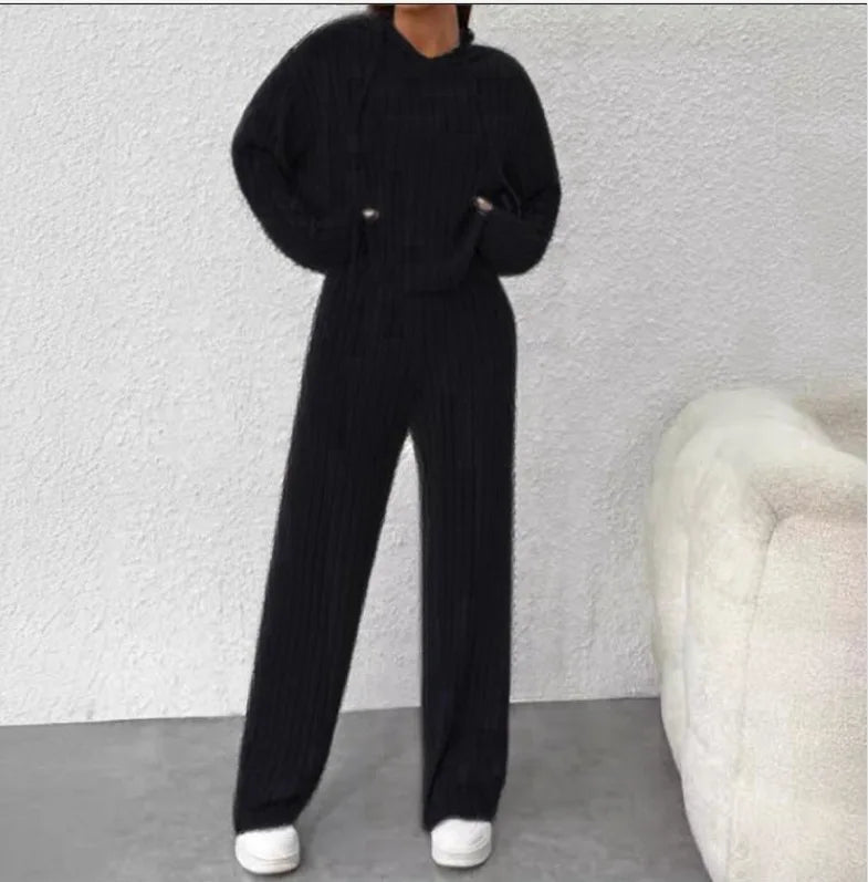 Person wearing a black outfit standing against a light gray wall with a white chair.