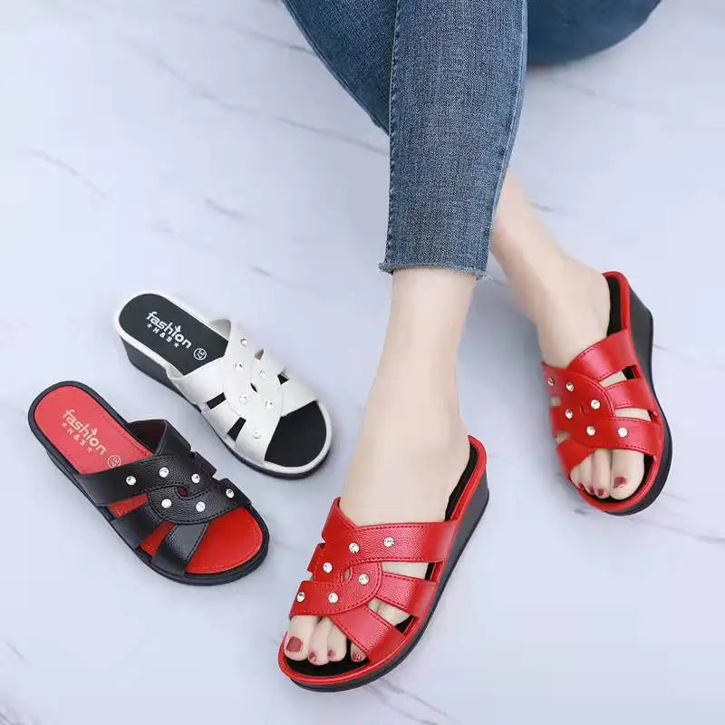 Red sandals with studded details worn by a person on a light gray floor.