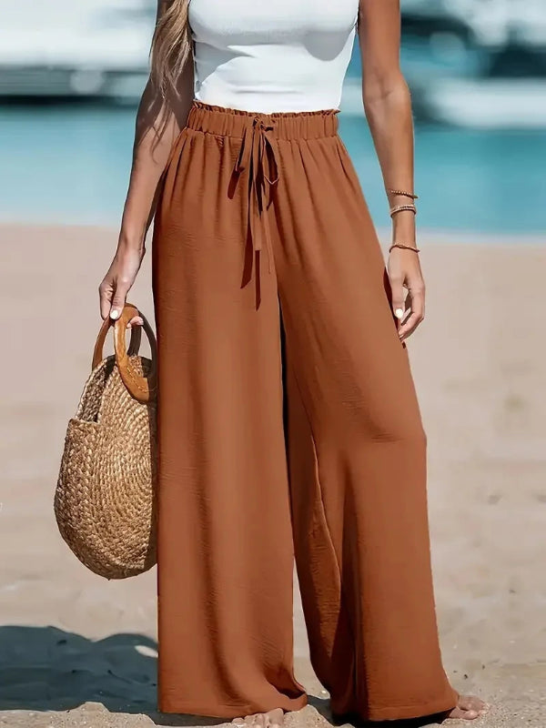 Person wearing brown wide-leg pants and a white top on a beach.