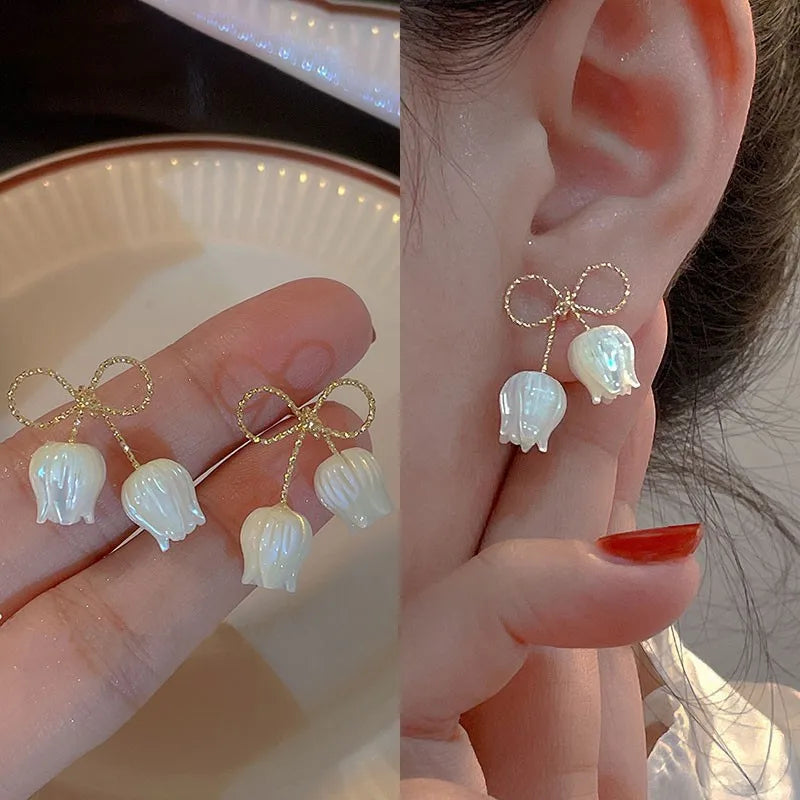 Pearl and bow-shaped earrings held by a hand with a blurred background