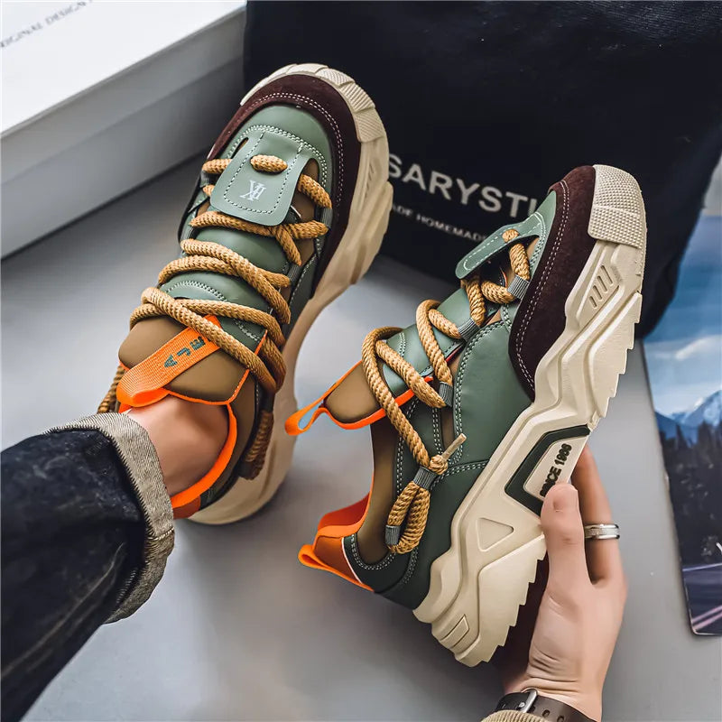 Pair of multicolored sneakers with orange accents worn by a person, on a light gray surface.