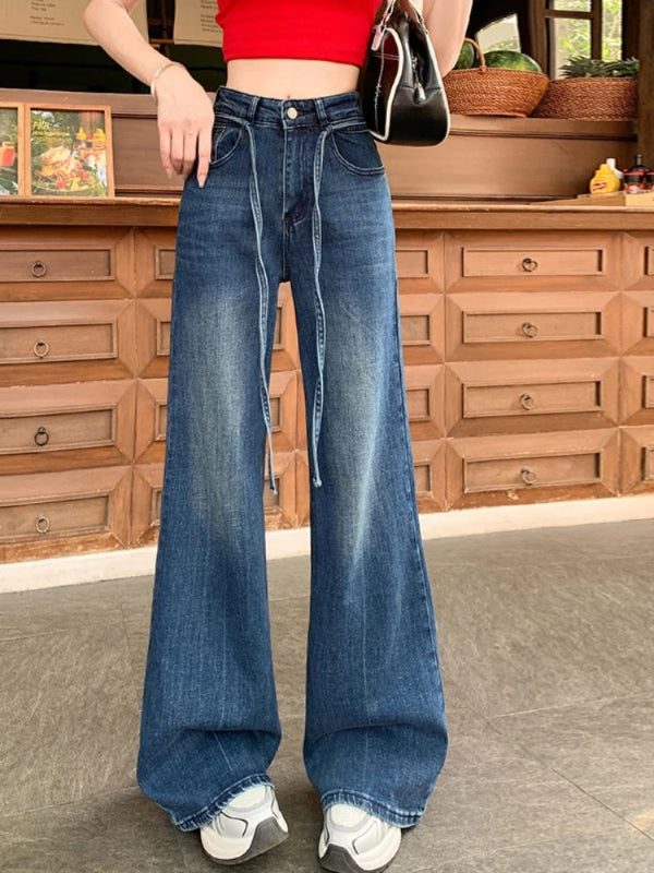 Person wearing blue wide-leg jeans with a red top in front of wooden furniture.