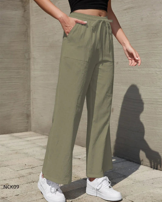Person wearing olive green pants and white sneakers against a concrete wall.