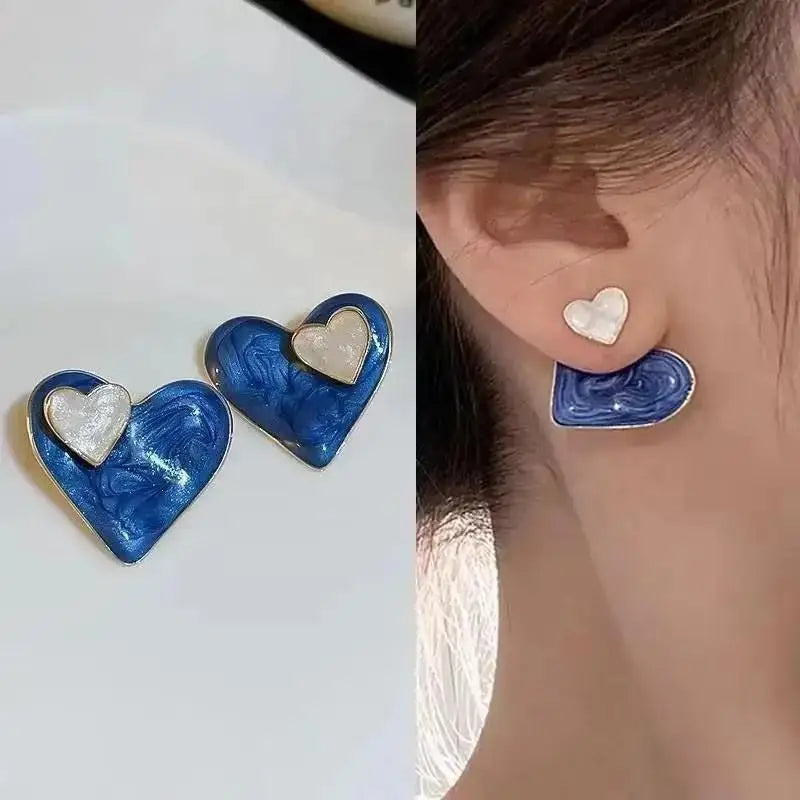 Heart-shaped earrings with blue and white design on a light background, worn by a person.