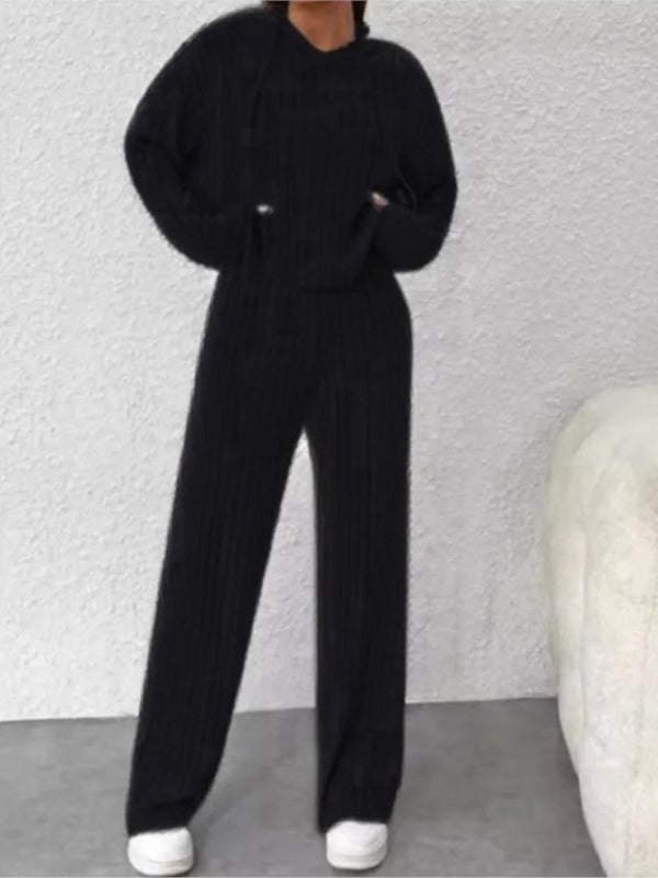 Person wearing a black outfit with white shoes against a textured gray wall.