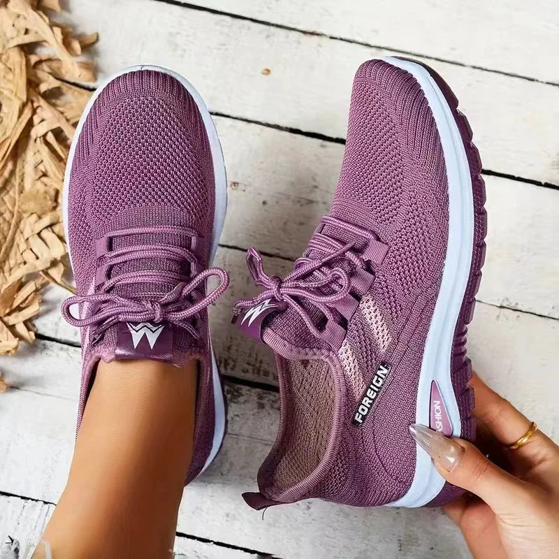 Purple running shoes with white soles held by a person on a wooden floor.