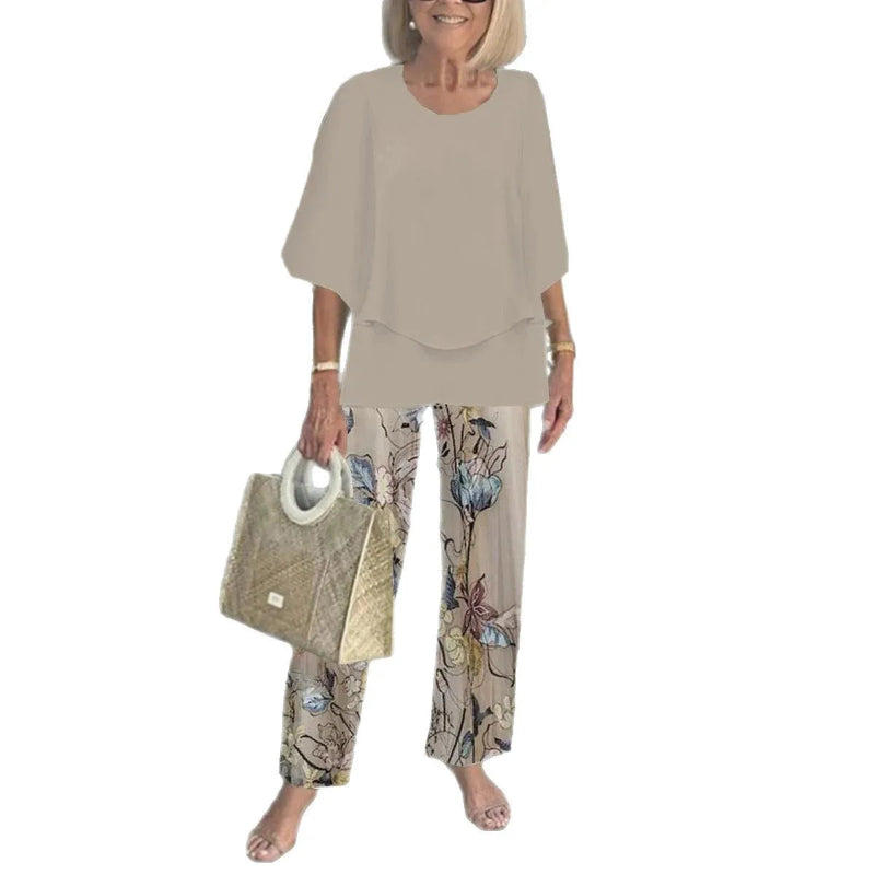 Woman wearing a beige outfit with floral pants and holding a beige handbag on a white background
