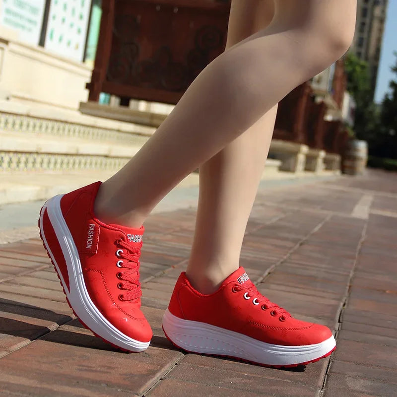Red sneakers with white soles worn on a person's feet, standing on a brick pavement.