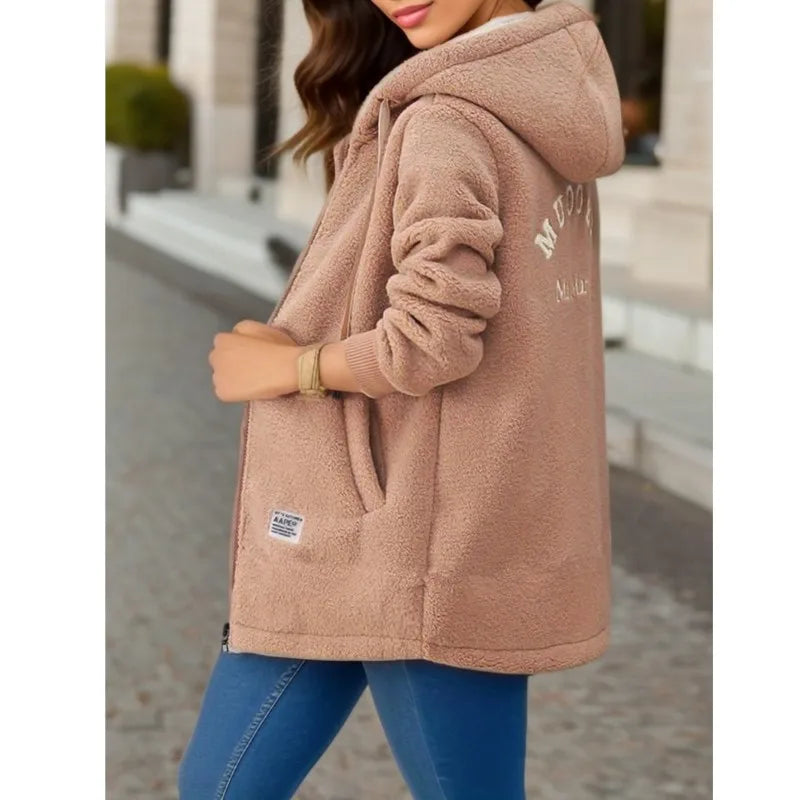 Person wearing a beige fleece jacket with a brand logo, standing outdoors.