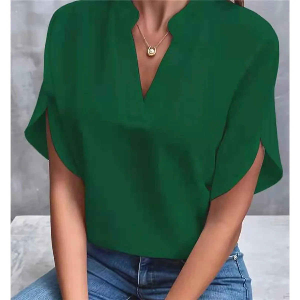 Green blouse with a V-neck and short sleeves worn by a person, sitting on a light-colored surface.