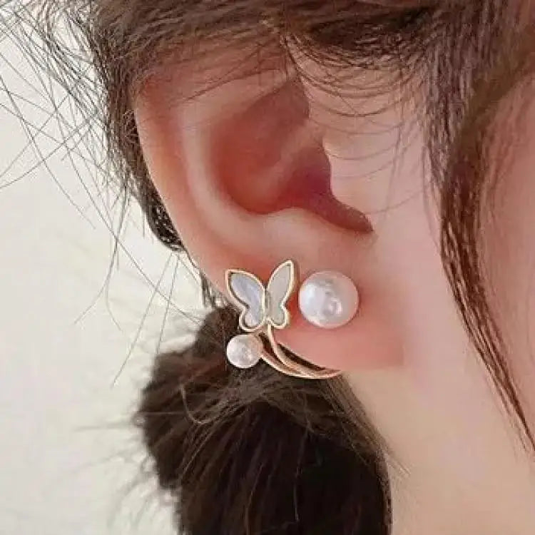 Butterfly-shaped earring with pearl details worn by a person.