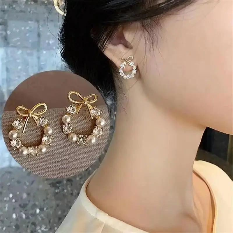 Gold hoop earrings with bow and pearl details worn by a person, with a close-up inset on a textured surface.