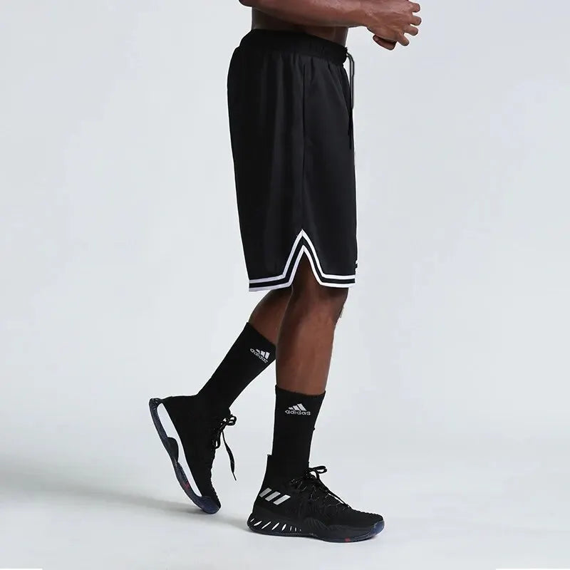 Person wearing black athletic shorts with a white stripe, black socks, and black sneakers on a light gray background.