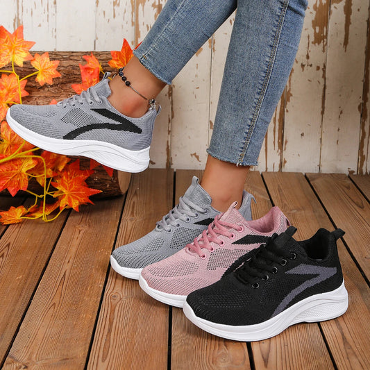 Four pairs of sneakers in gray, pink, and black on a wooden floor with a floral arrangement.