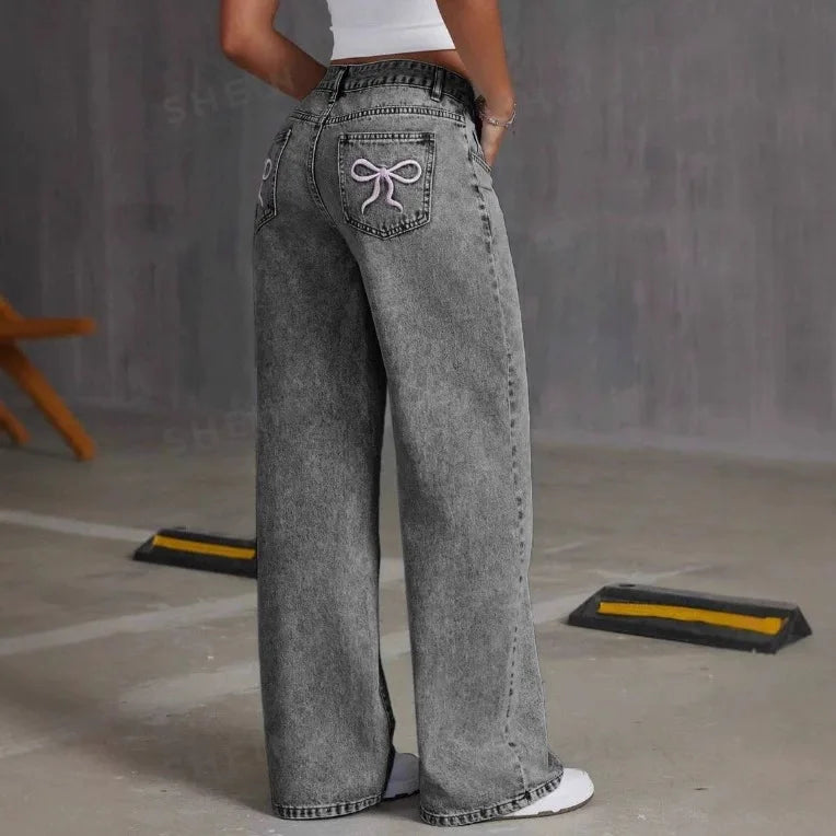 Person wearing gray wide-leg jeans with a decorative bow on the back pocket against a plain background.