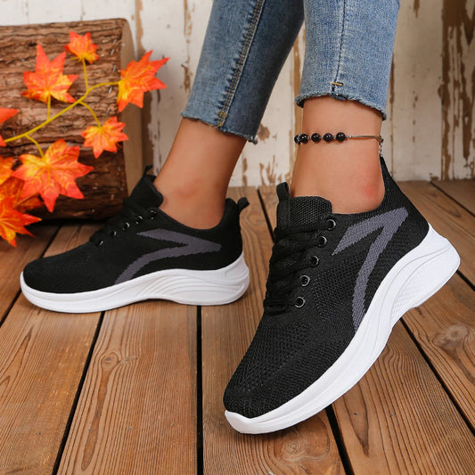 Black athletic shoes with white soles worn by a person on a wooden floor.