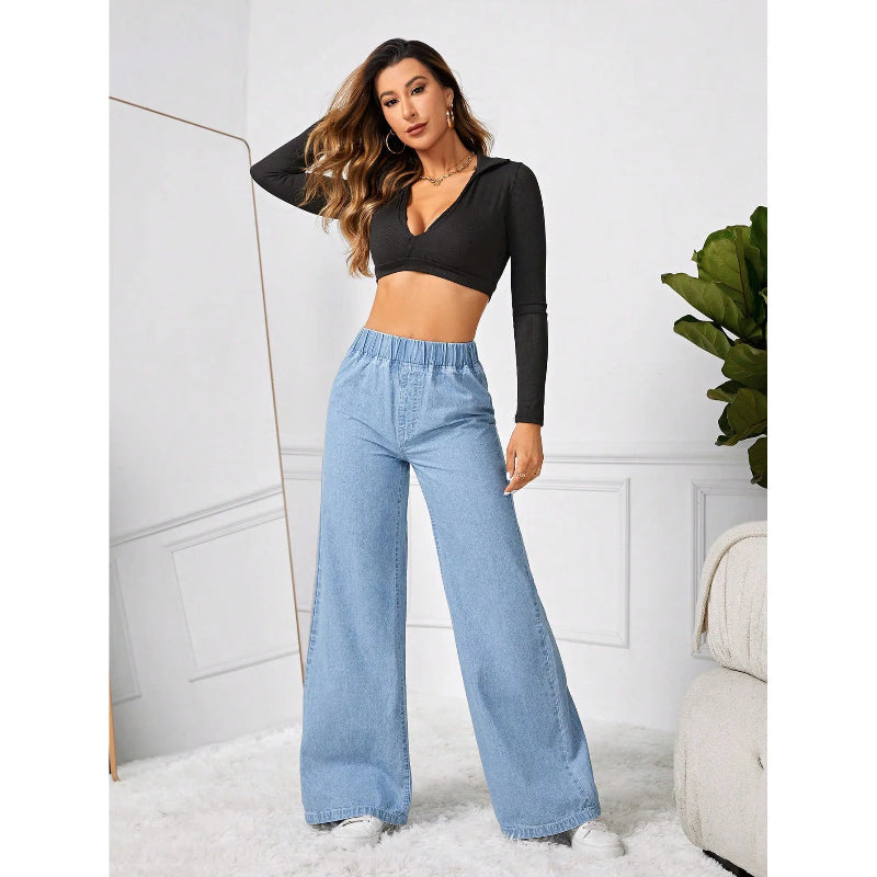 Woman wearing a black long-sleeve crop top and light blue high-waisted jeans in a minimalistic room.