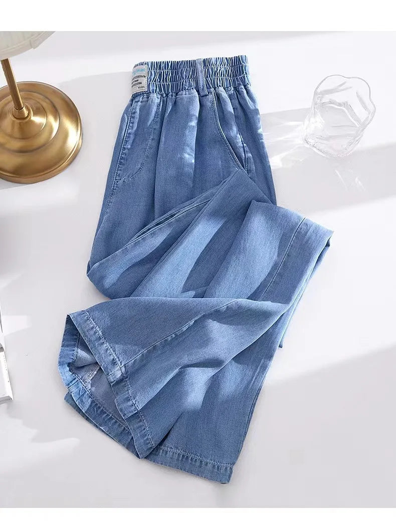 Folded blue denim pants on a white surface with a gold lamp in the background
