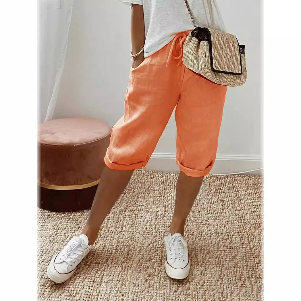 Person wearing orange pants and white sneakers with a straw bag, standing on a carpeted floor.