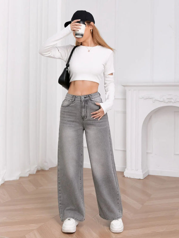 Person wearing a white long-sleeve top, gray wide-leg jeans, and a black cap, holding a coffee cup.