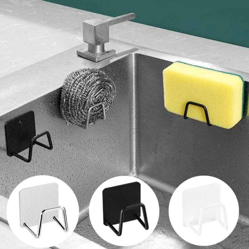 A stainless steel self-adhesive wall hook designed to hold sponges, mounted on a kitchen sink corner. The image shows the hook in a silver color and also includes variants in black and white.