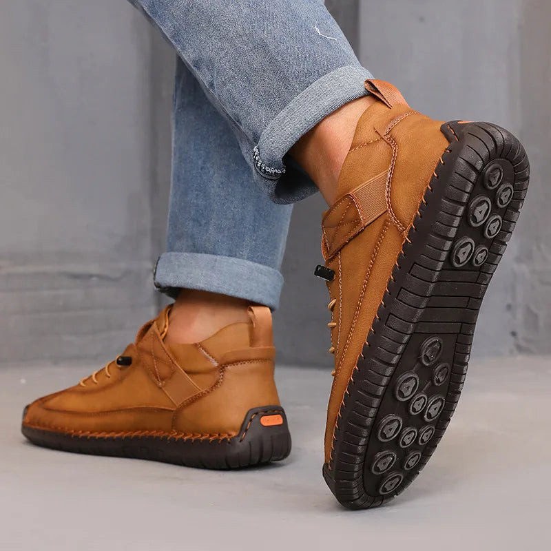 Brown shoes with black soles worn with rolled-up jeans on a gray background