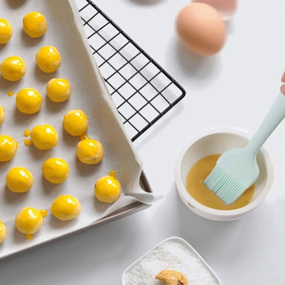 Baking process with yellow spherical cookies on a tray, eggs, and a brush with a bowl of egg wash.