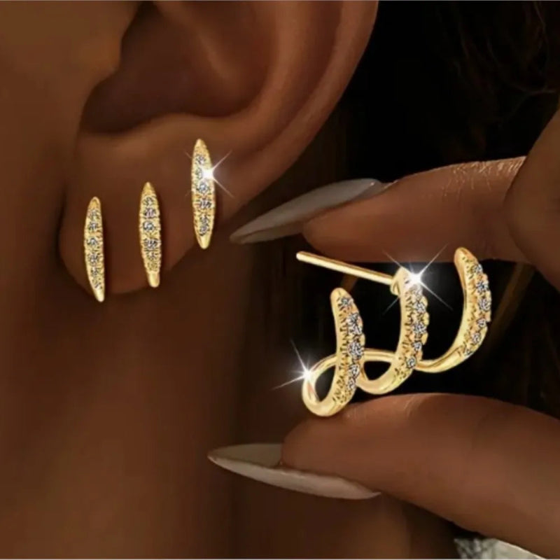 Gold earrings being worn and held by a hand against a dark background