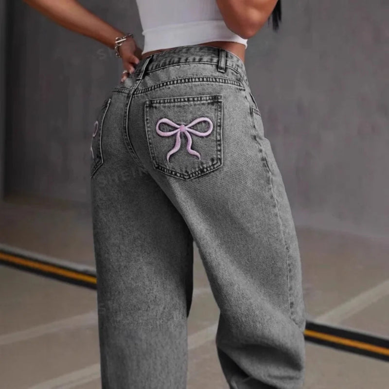 Gray jeans with a pink bow design on the back pocket against a neutral background
