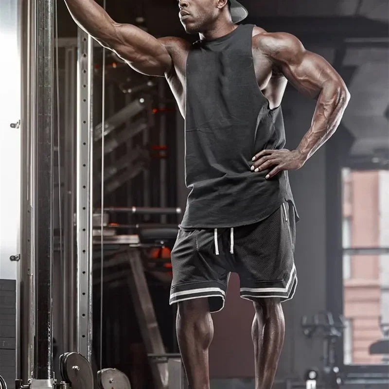 Muscular man in black tank top and shorts posing in a gym setting
