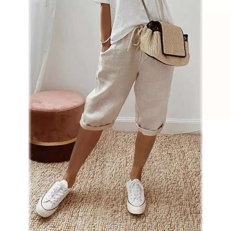 Person wearing white sneakers, light-colored pants, and a straw bag on a carpeted floor.