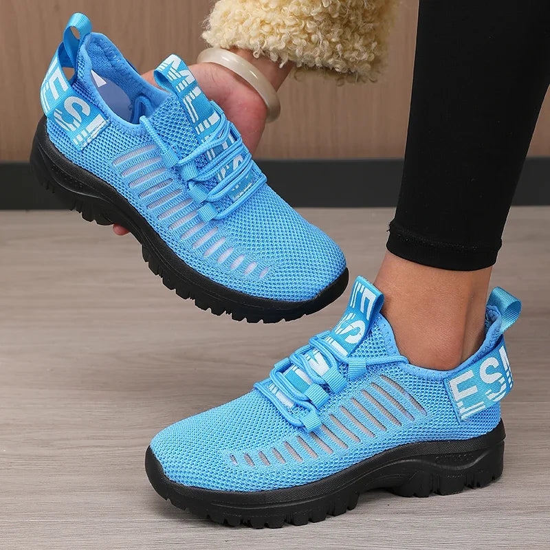 Blue athletic shoes with black soles worn by a person on a wooden floor.