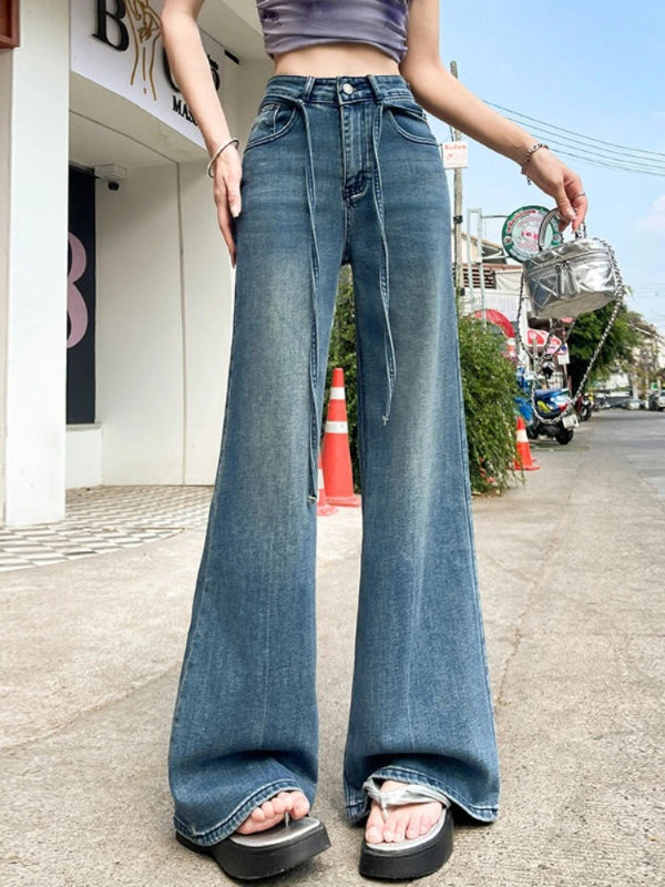 Person wearing blue flared jeans on a street with buildings and traffic cones in the background.