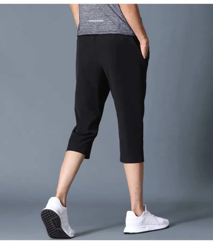 Person wearing black capri pants and white sneakers on a gray background