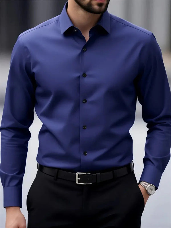 Man wearing a blue dress shirt with black buttons and black pants against a neutral background