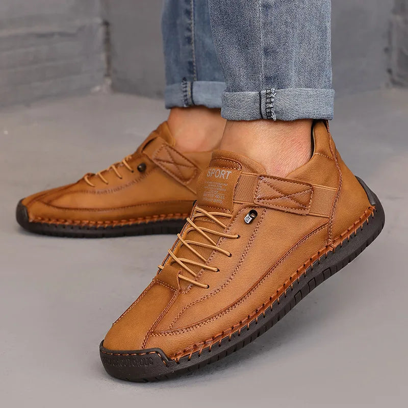 Brown leather shoes worn with rolled-up jeans on a gray floor.