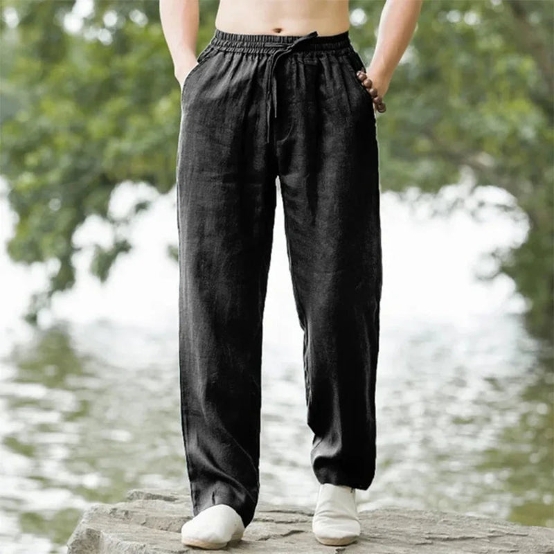 Person wearing black pants standing by a body of water with greenery.
