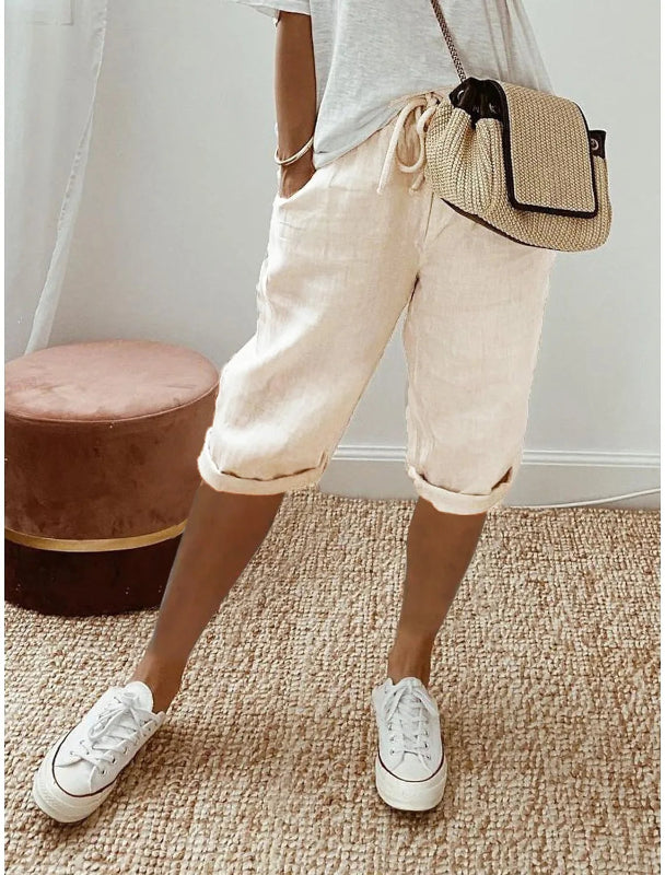 Person wearing beige shorts, white sneakers, and a beige crossbody bag on a carpeted floor.