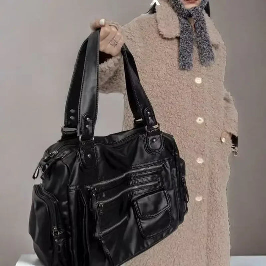 Person holding a black leather handbag against a neutral background