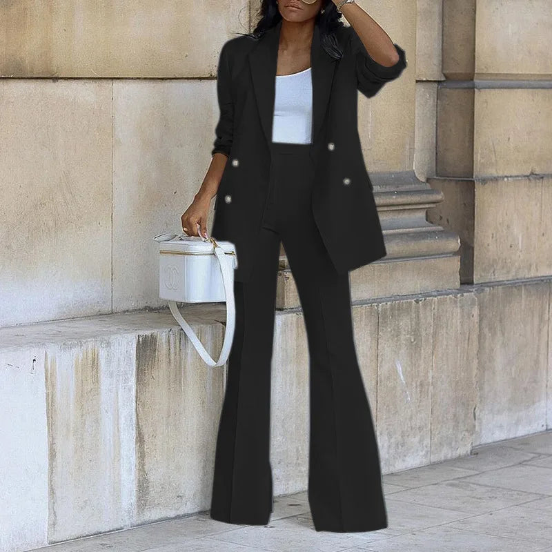 Woman in black suit and white top standing against a stone wall.