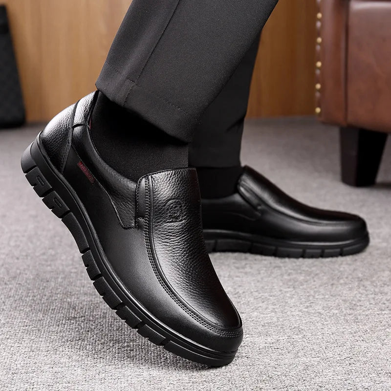 Black leather shoes worn with black pants on a gray floor.