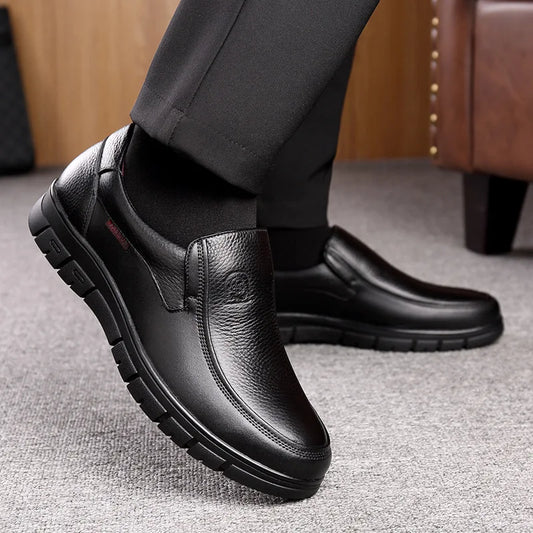 Black leather shoes worn with black pants on a gray floor.