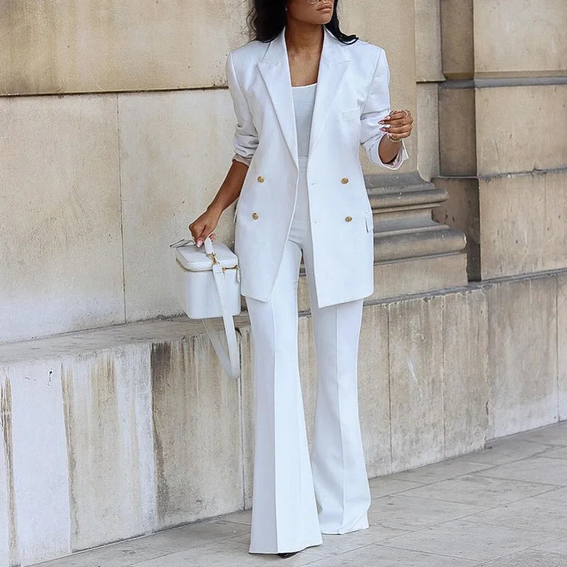 Person wearing a white suit standing against a stone wall.
