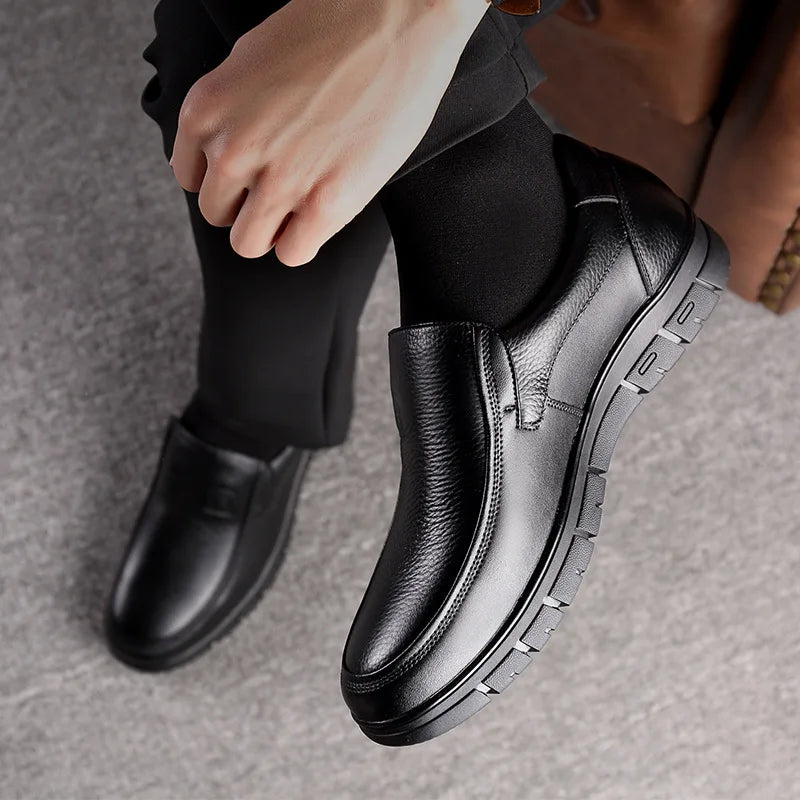 Black leather shoes worn with black pants on a neutral background