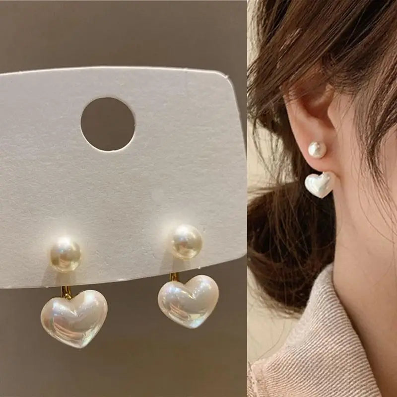 Heart-shaped pearl earrings on a display card and worn by a person.