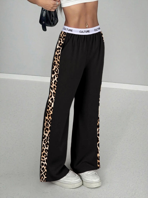 Black wide-leg pants with leopard print side panels worn by a person on a gray background